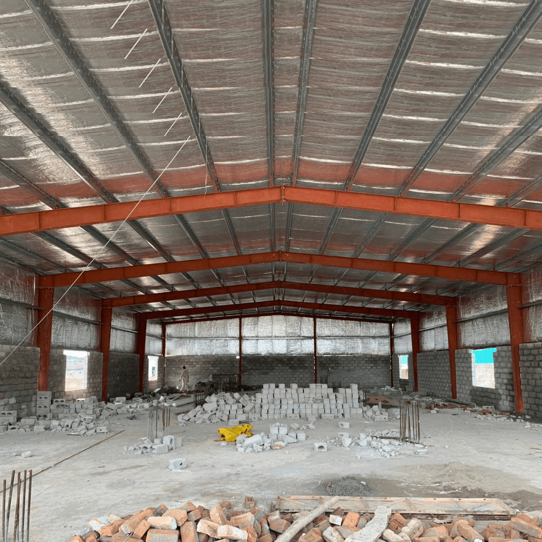 Interior of a large unfinished industrial building with metal beams and stacks of concrete blocks.