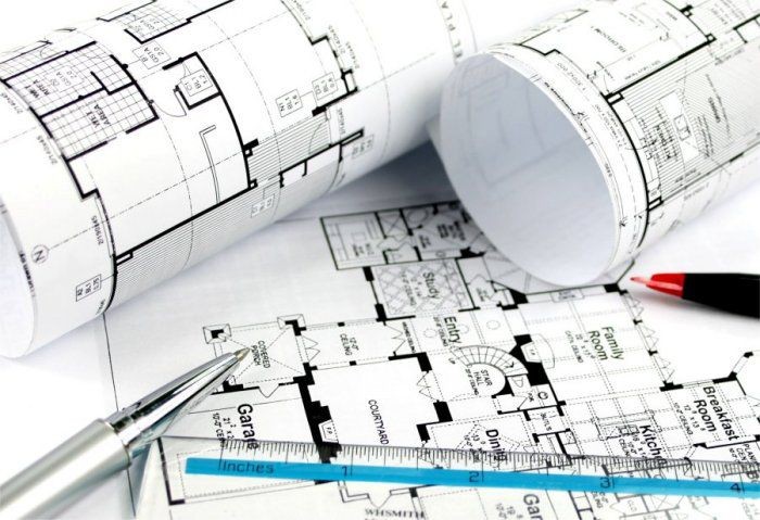 Rolled architectural blueprints with a pen and ruler on top of floor plans.