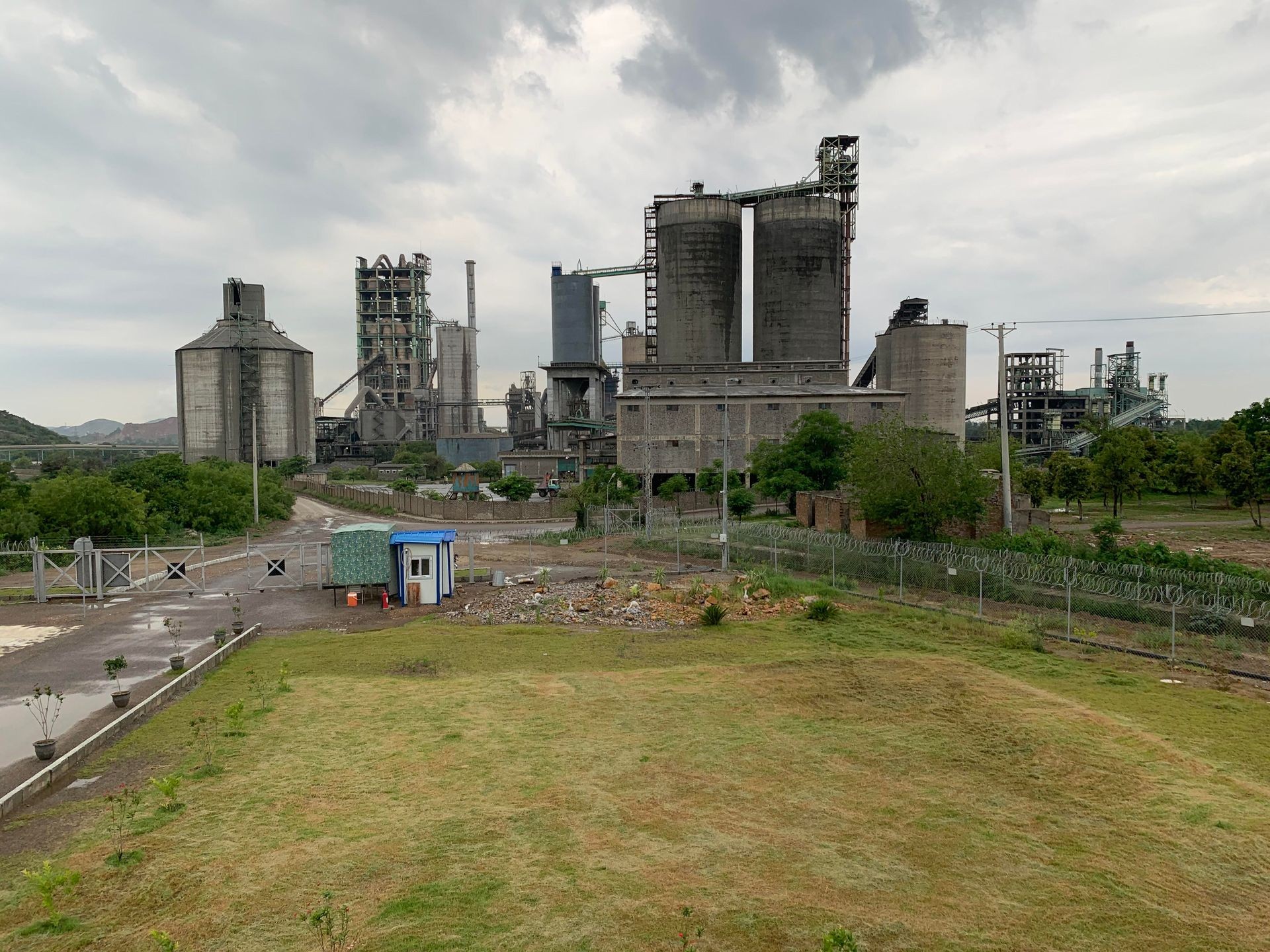 Outdoor view of an industrial facility with large silos, connecting structures, and surrounding green landscape.